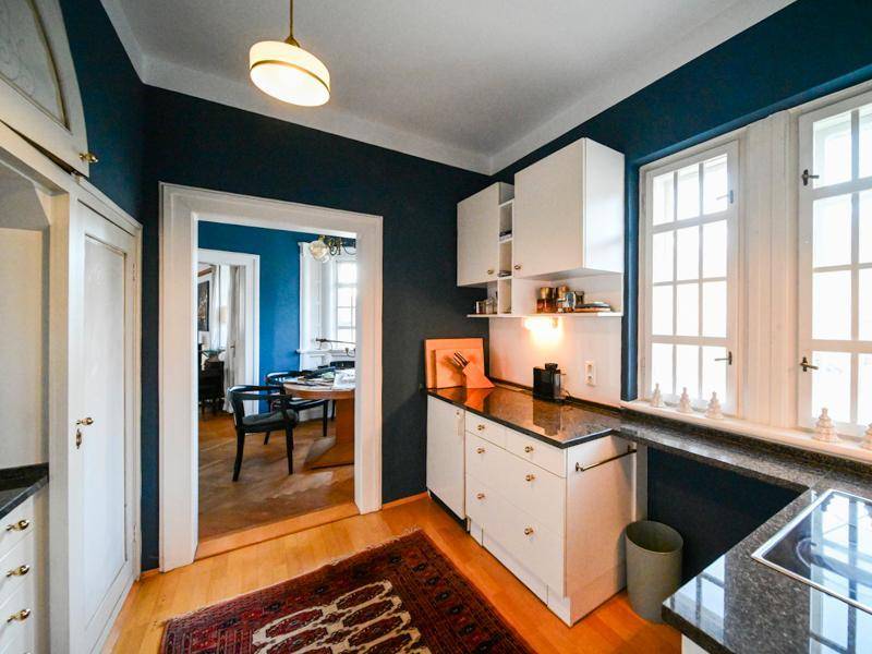 Küche mit dunkelblauen Wänden, weißen Schränken und Holzboden, Blick ins Esszimmer.