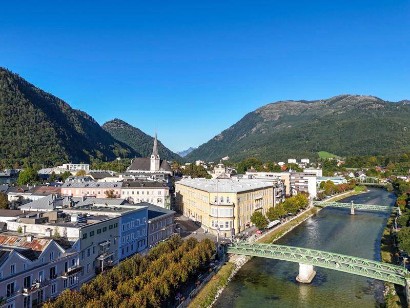 Luftaufnahme einer Stadt mit Fluss, Brücke und Kirchturm, eingebettet in eine Berglandschaft.