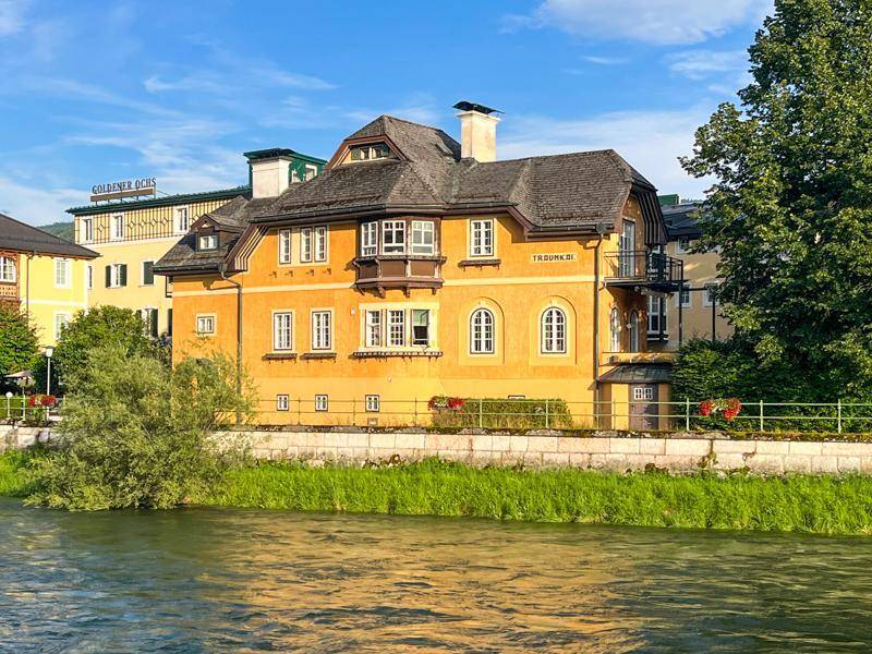 Historisches gelbes Gebäude am Flussufer mit Bergblick und traditioneller Architektur.