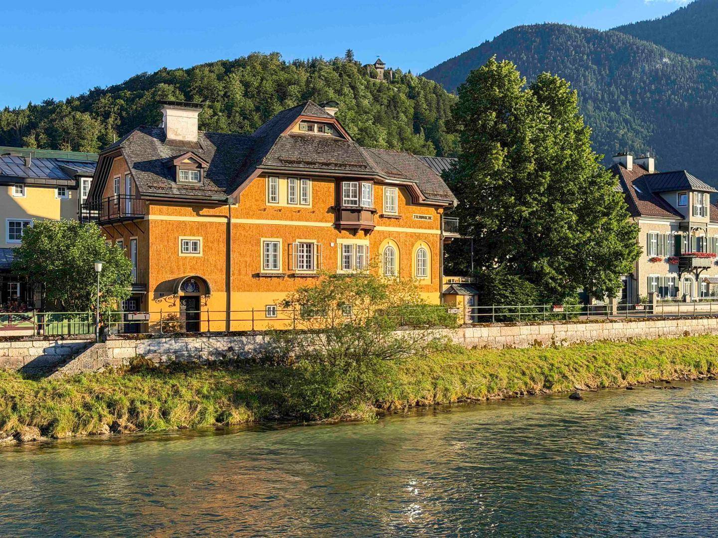Historisches gelbes Gebäude am Flussufer mit Bergblick und traditioneller Architektur.