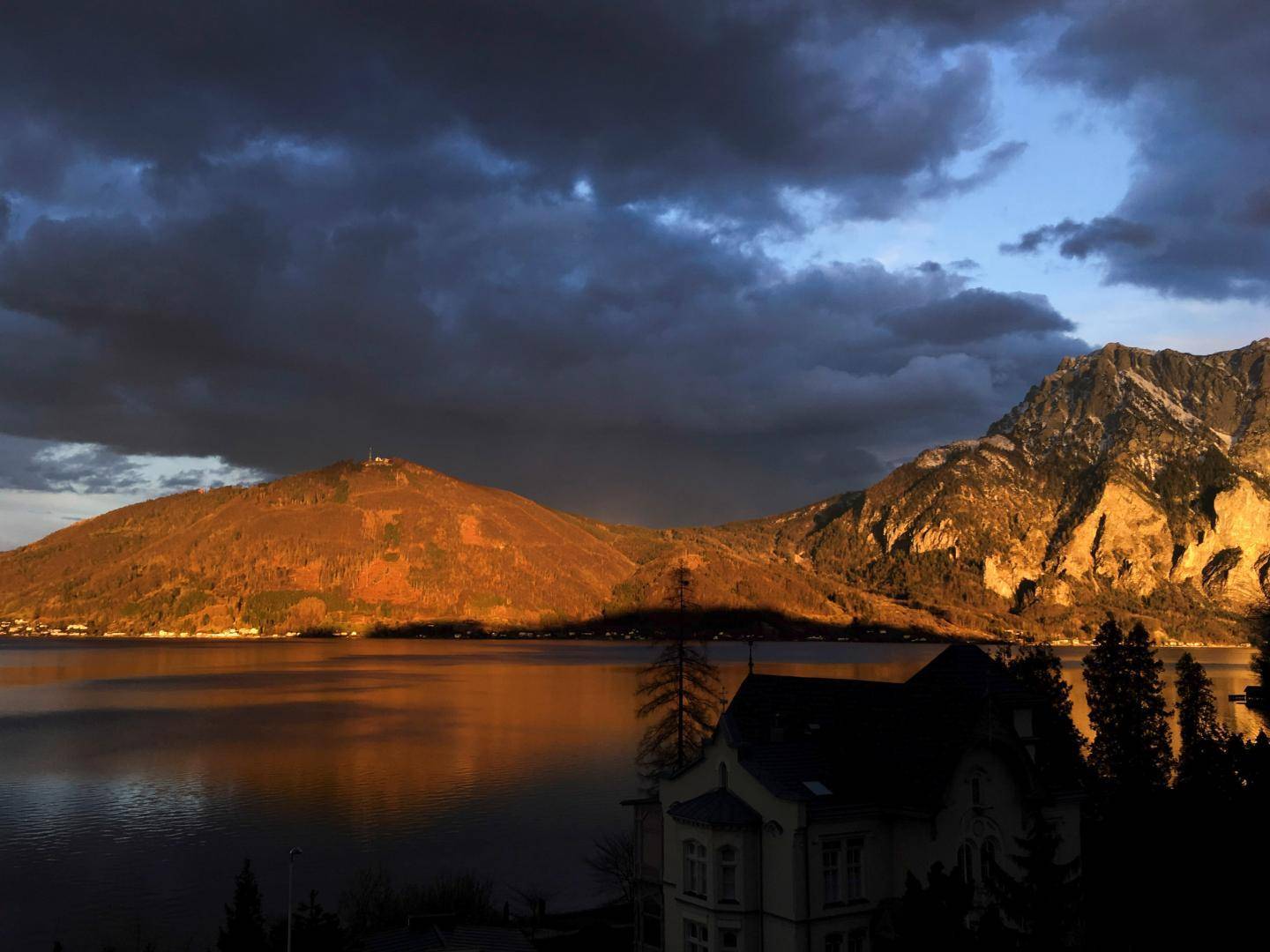 Atemberaubender Blick auf den See und die Berge im warmen Abendlicht unter einem bewölkten Himmel.