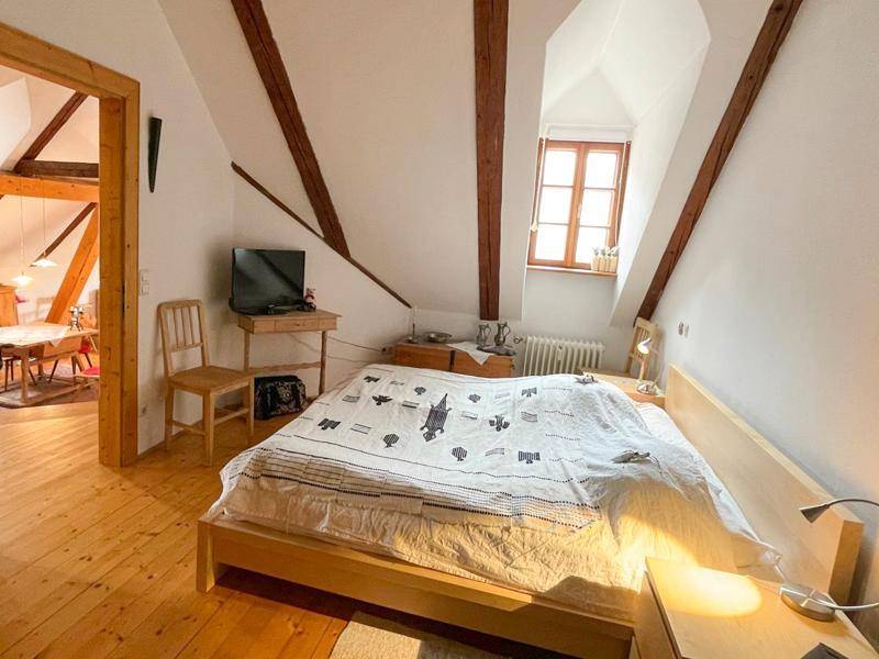 Gemütliches Schlafzimmer im Dachgeschoss mit Holzbalken, Holzboden und einem Fenster.