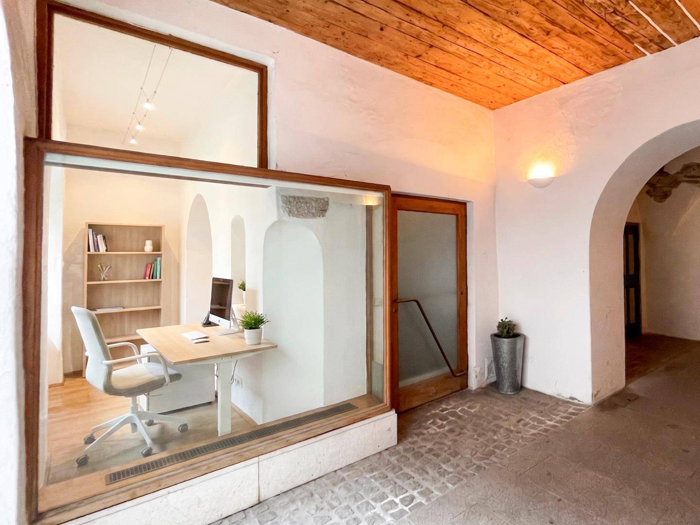 Modernes Büro mit Holzboden und Glaswand, gelegen in einem historischen Gebäude mit Gewölbegang.