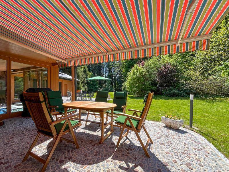 Überdachte Terrasse mit Gartenmöbeln und bunter Markise, umgeben von viel Grün.