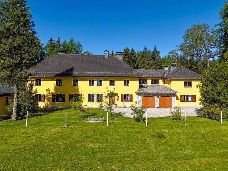 Großes gelbes Landhaus mit dunklem Dach und zwei Garagentoren, umgeben von Grünflächen.