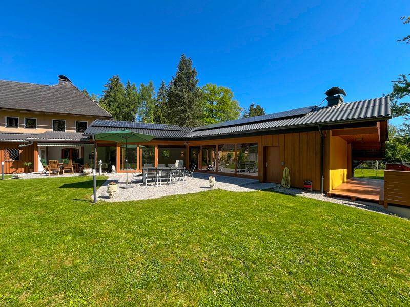 Modernes Gebäude mit großen Glasfronten und Solarpaneelen, angrenzend an eine Grünfläche.