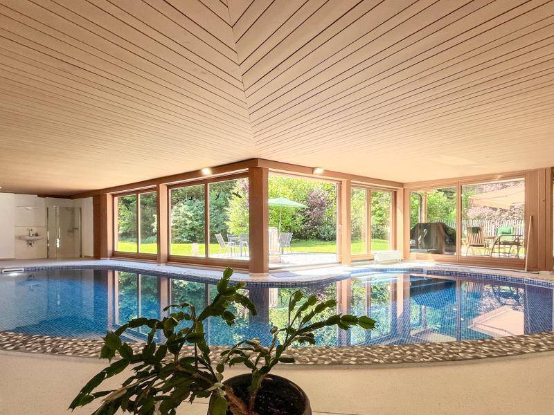 Großzügiger Innenpoolbereich mit Holzdecken und großen Fenstern zum Garten.
