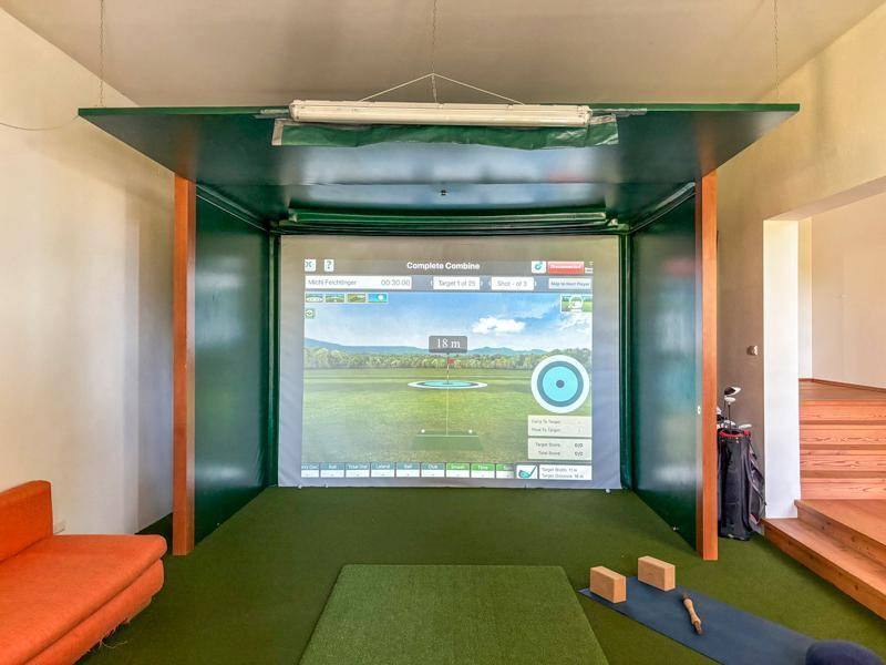 Innenraum mit Golfsimulator und Kunstrasen für sportliche Aktivitäten.