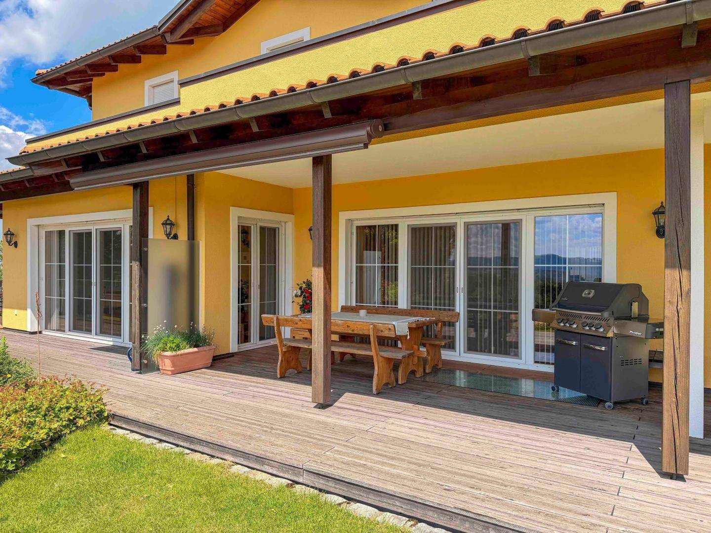 Große Holzterrasse mit Esstisch, Grill und Zugang zum Gartenbereich.