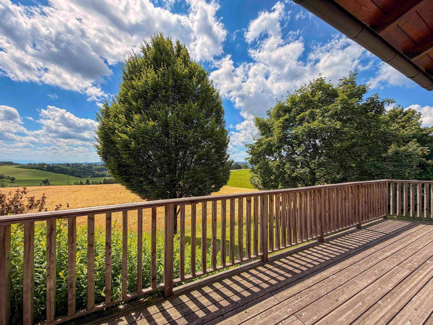 Geräumiger Holzbalkon mit Geländer und weitem Blick über Felder und Bäume.