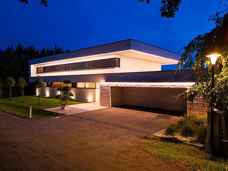 Moderne Villa bei Nacht mit beleuchteter Fassade und integrierter Garage.