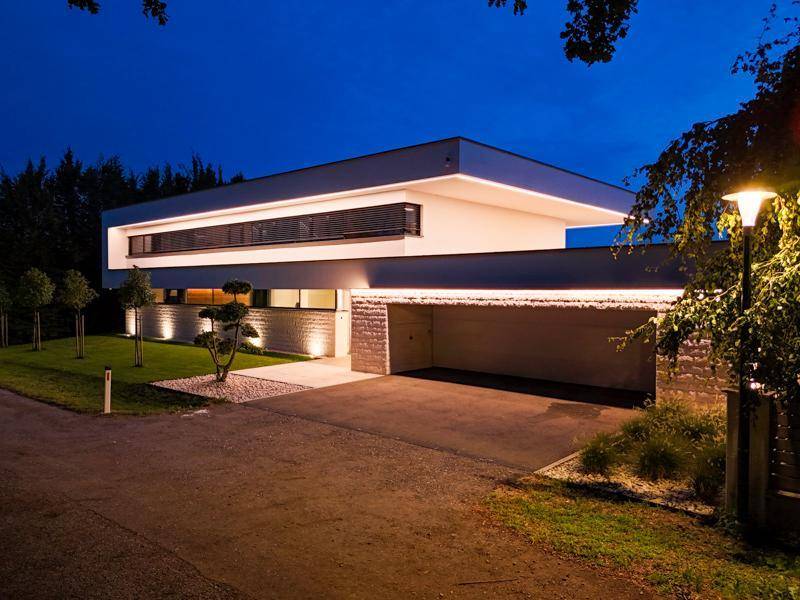 Moderne Villa bei Nacht mit beleuchteter Fassade und integrierter Garage.