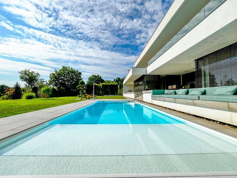 Moderne Architektur mit großem Außenpool und weitläufigen Terrassenflächen unter blauem Himmel.