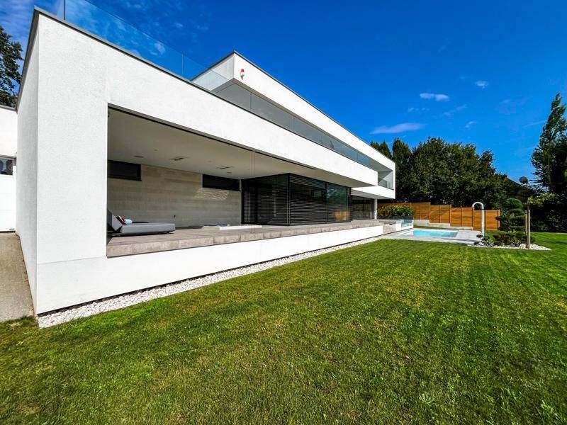 Seitliche Ansicht der modernen Villa mit gepflegtem Rasen und Poolbereich.