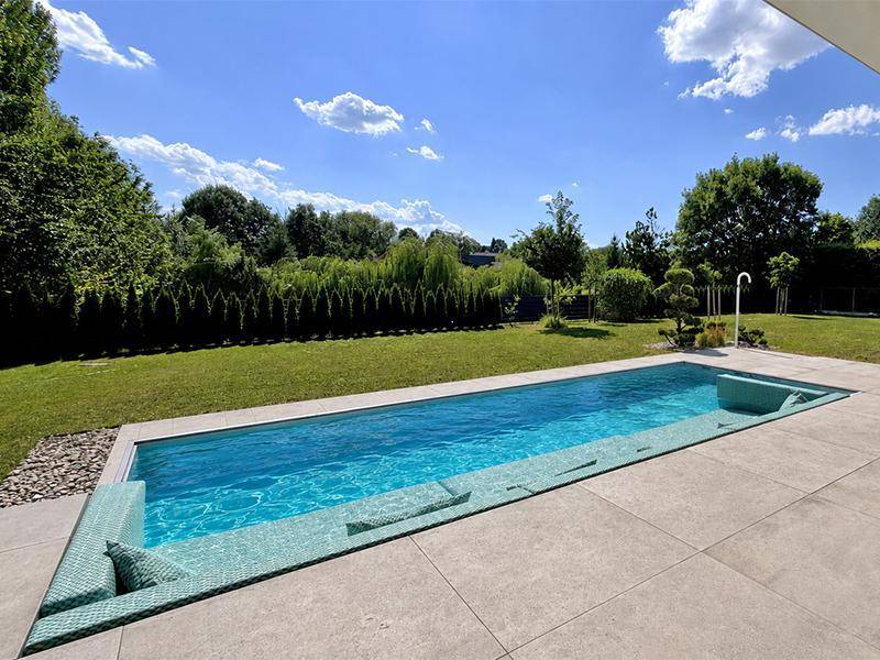 Gepflegter Gartenbereich mit langem Swimmingpool und grüner Hecke unter strahlendem Himmel.