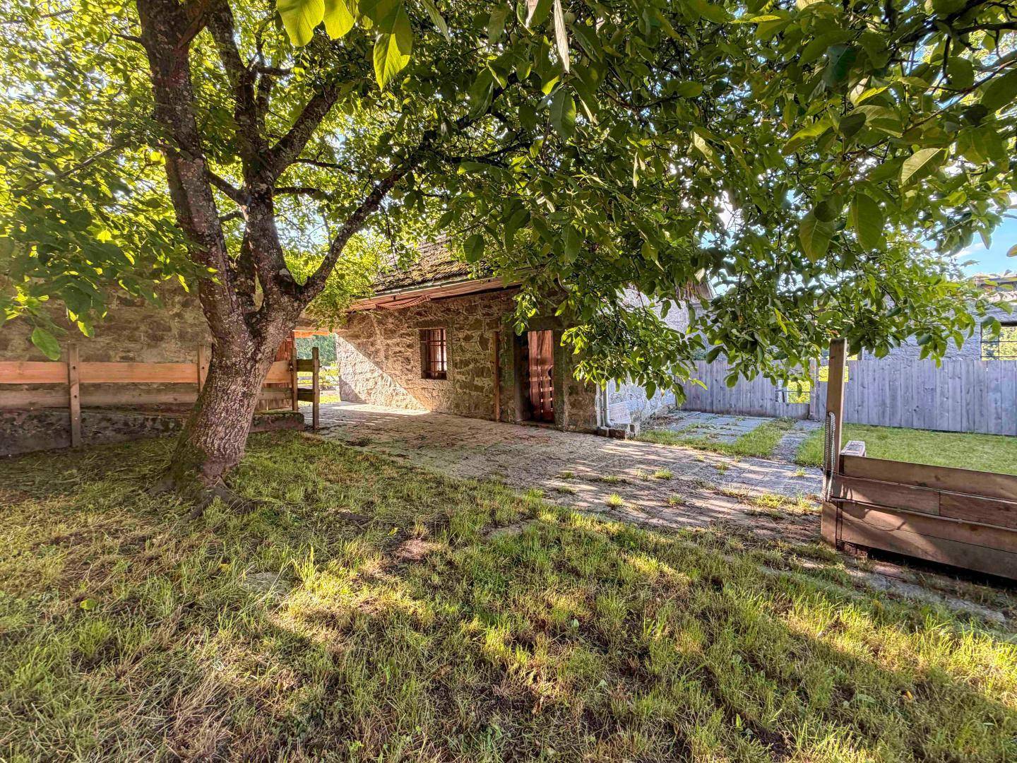 Kleines Steinhaus im Gartenbereich mit altem Baum und sonniger Atmosphäre, umgeben von Grün.