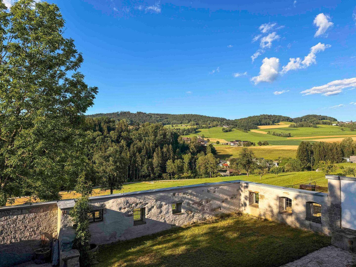 Weitläufiger Blick auf das Anwesen und die umliegende grüne Hügellandschaft unter blauem Himmel.