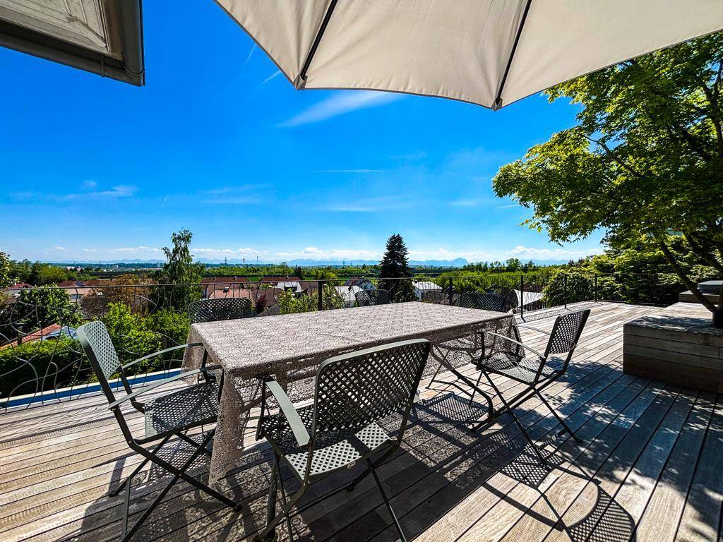 Sonnige Holzterrasse mit Esstisch und weitem Blick über die Landschaft und die Stadt.