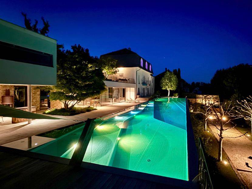 Beleuchtetes Anwesen bei Nacht mit langem Infinity-Pool und stimmungsvoller Gartenbeleuchtung.