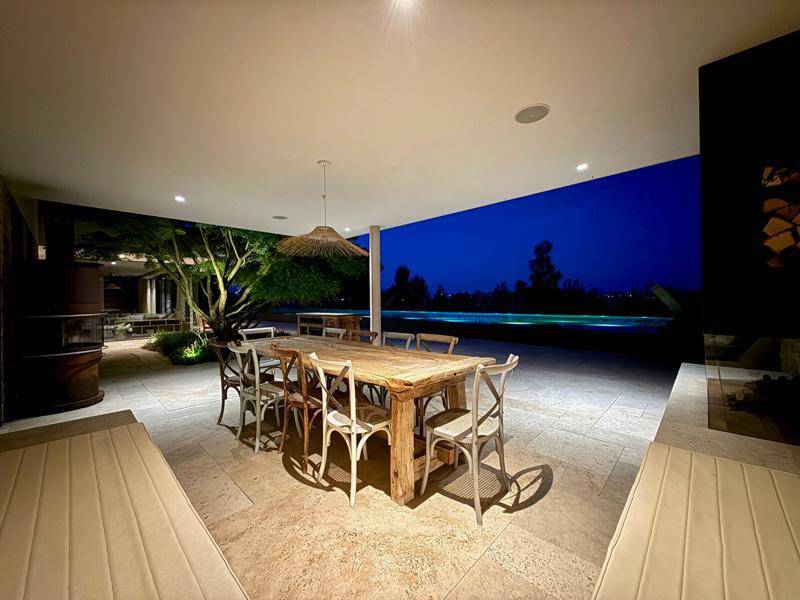 Stimmungsvoll beleuchtete überdachte Terrasse bei Nacht mit Esstisch und Poolblick.