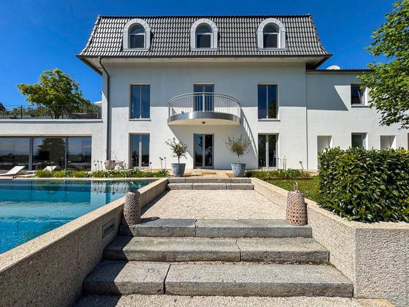 Elegante Fassade des Hauses mit Mansarddach, umgeben von einem Pool und gepflegter Landschaft.
