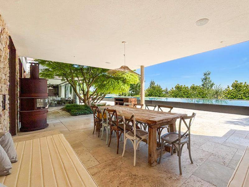 Geräumige überdachte Terrasse mit rustikalem Esstisch und Blick auf den Infinity-Pool.