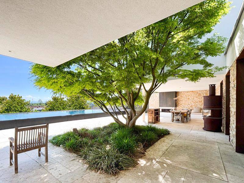 Überdachte Terrasse mit einem großen Baum in der Mitte und Blick auf den Infinity-Pool.
