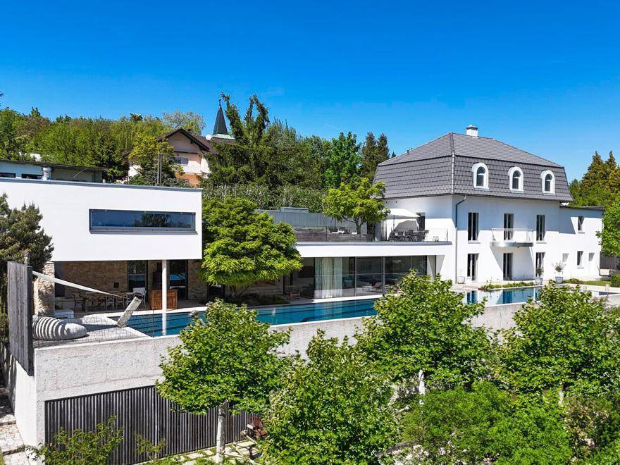 Architektonisch ansprechendes Anwesen mit zwei Gebäudeteilen, großem Pool und üppiger grüner Umgebung.