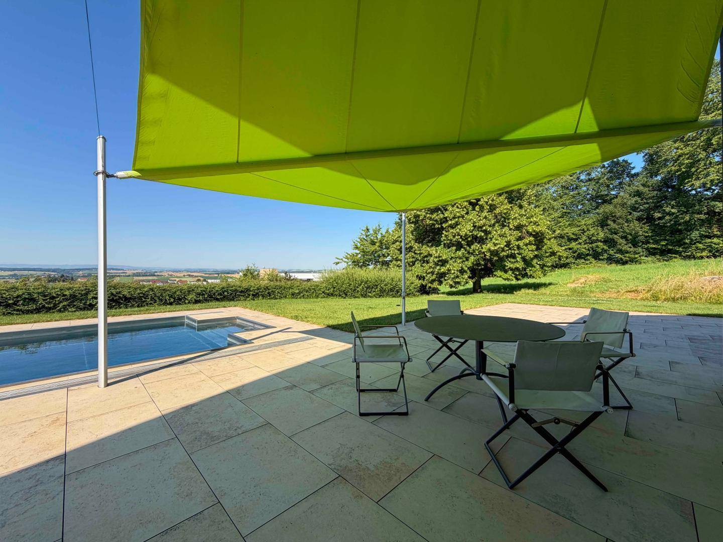 Sonniger Terrassenbereich mit Outdoor-Möbeln, Sonnensegel und angrenzendem Pool.