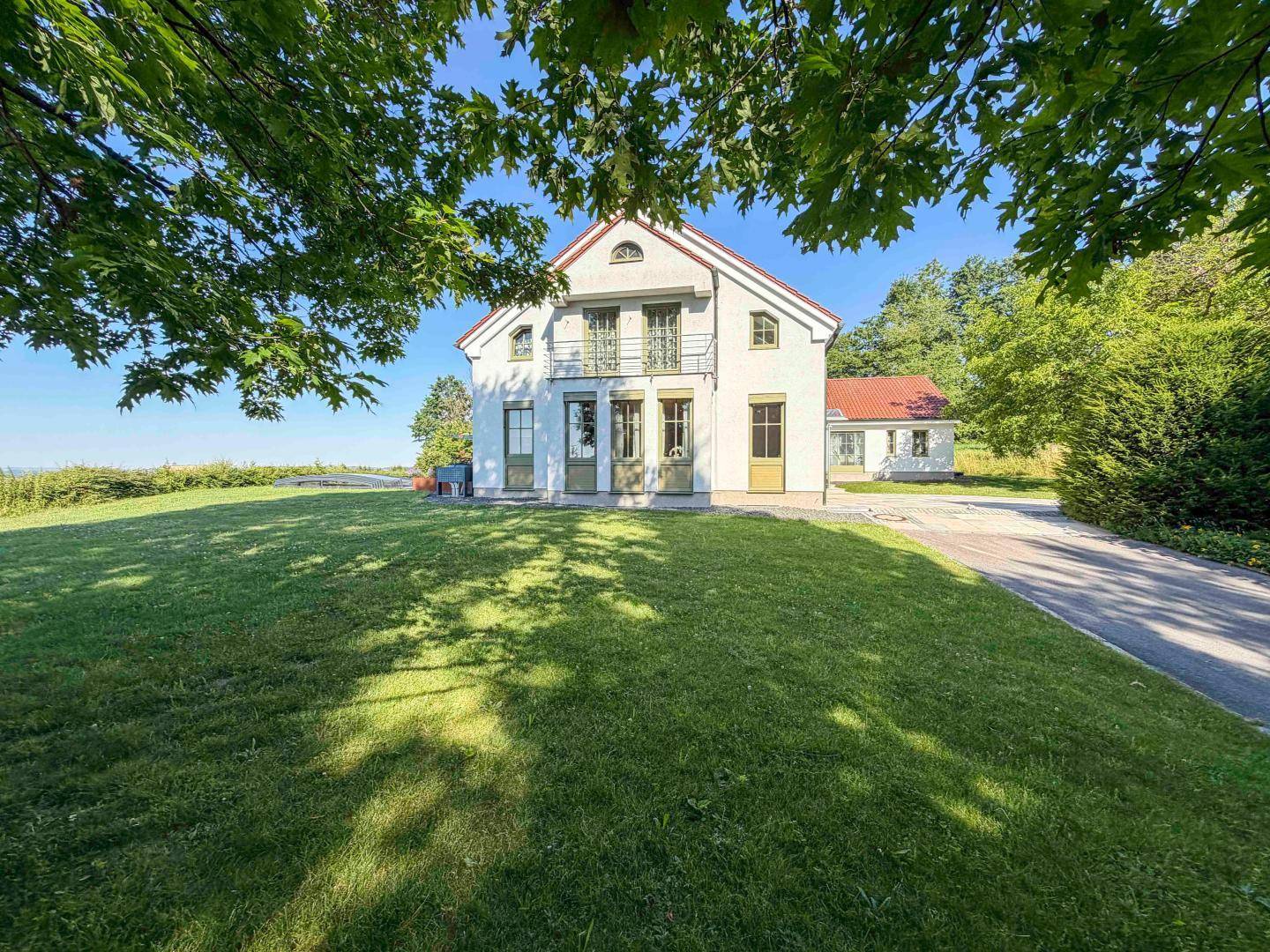 Elegantes Landhaus mit gepflegtem Rasen und altem Baumbestand unter blauem Himmel.