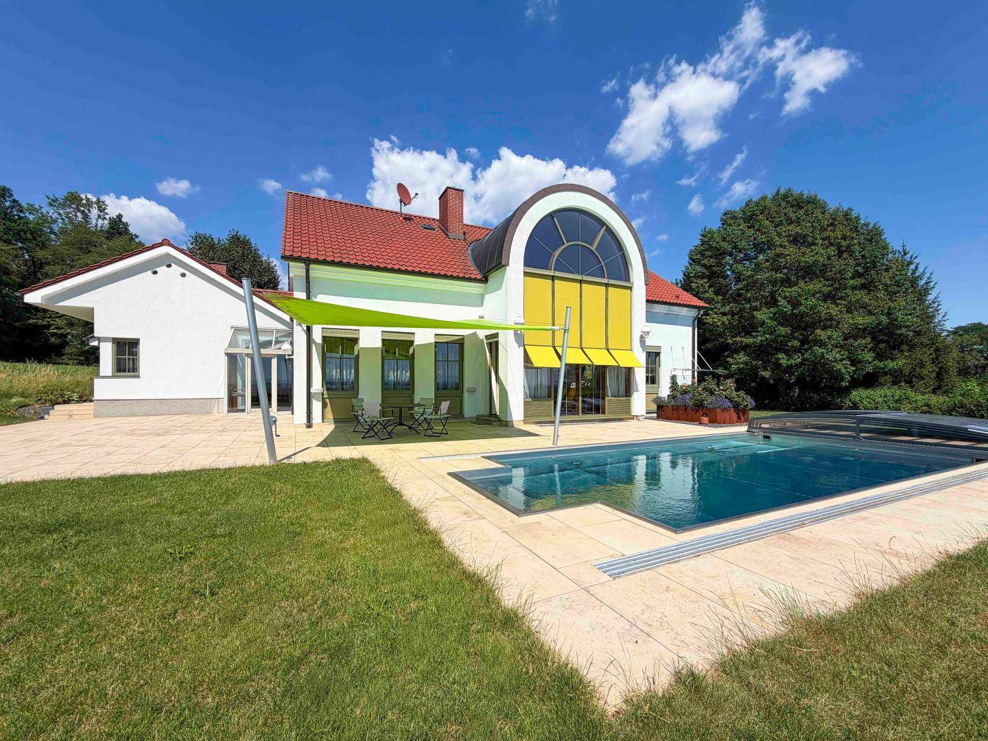 Außenbereich mit großem Pool, gepflasterter Terrasse und Sonnensegel vor dem Haus.