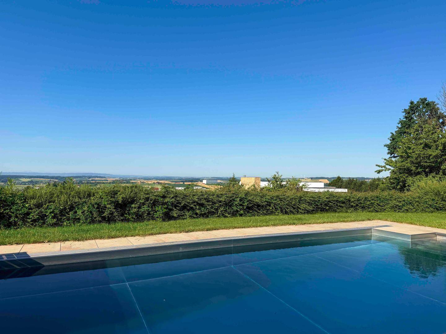 Infinity-Pool mit weitem Blick über die grüne Landschaft unter blauem Himmel.