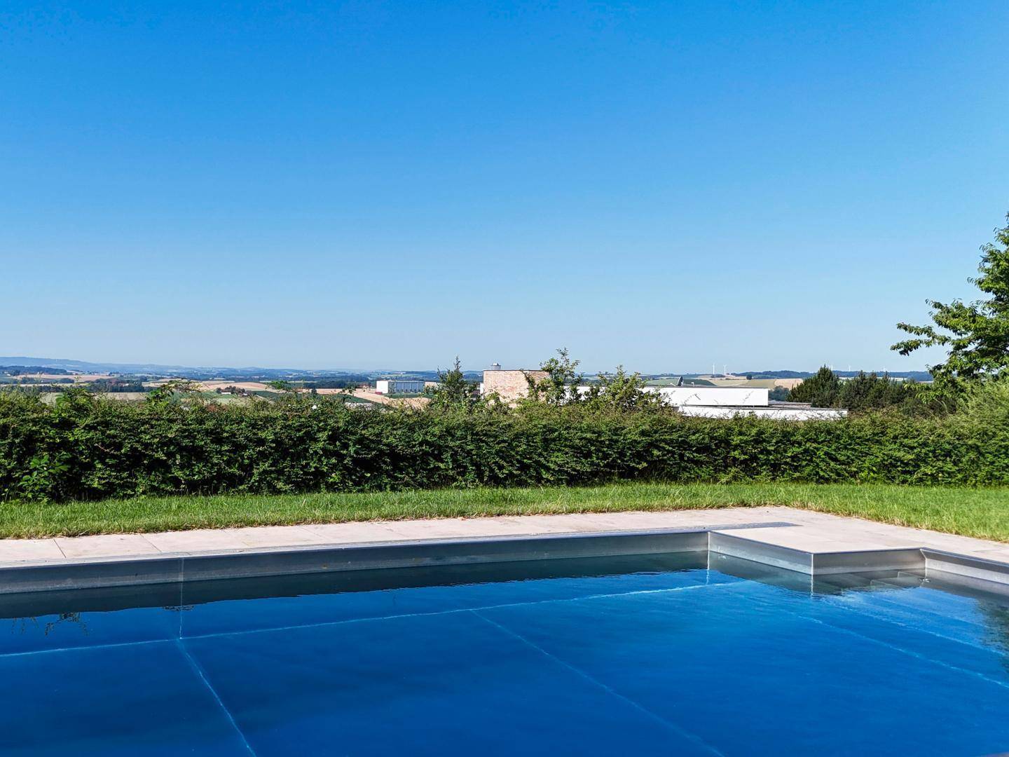 Blauer Pool mit weitem Panoramablick über die hügelige Landschaft an einem sonnigen Tag.