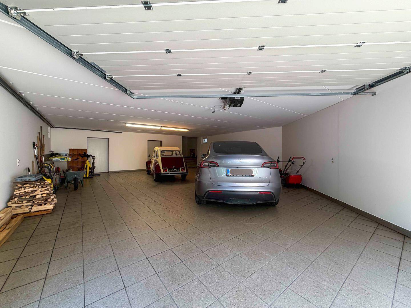 Geräumige Garage mit Fliesenboden, Platz für mehrere Fahrzeuge und Stauraum.