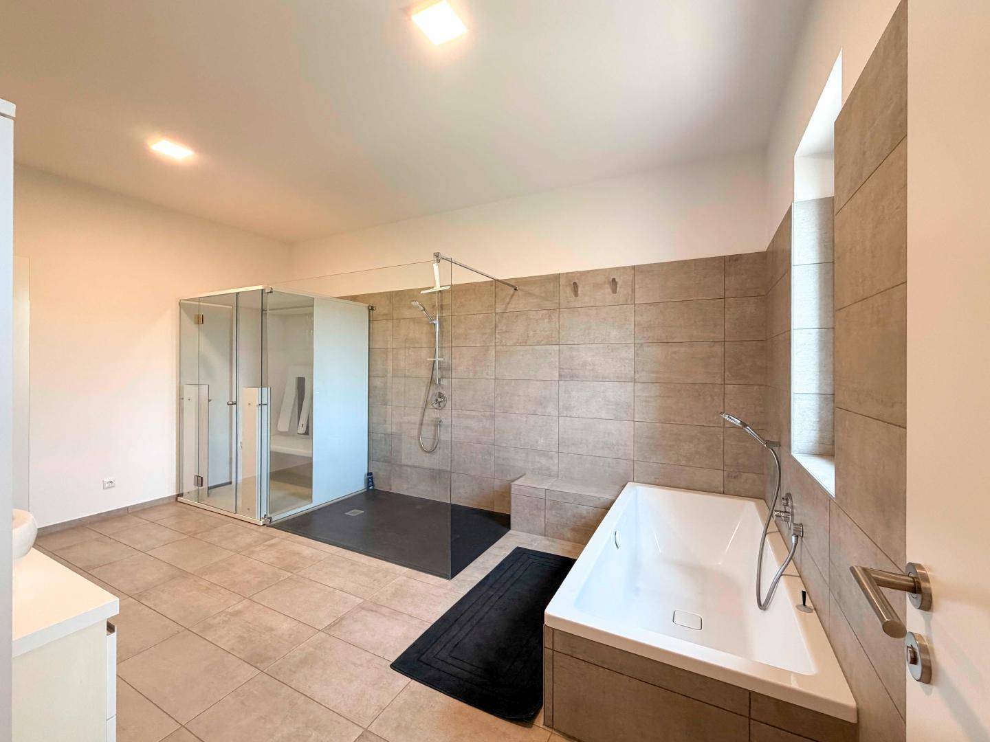 Modernes Badezimmer mit großer begehbarer Dusche, Badewanne und hellen Fliesen.