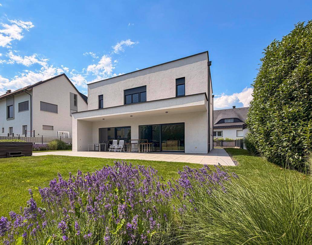 Moderne Architektur des Hauses mit weißer Fassade, großer Terrasse und gepflegtem Garten.