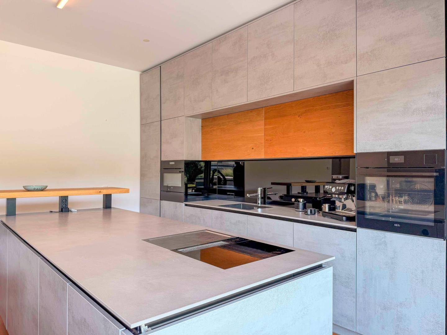 Hochmoderne Küche mit grauen Fronten, Holzdetails, Kochinsel und integrierten Premium-Geräten.