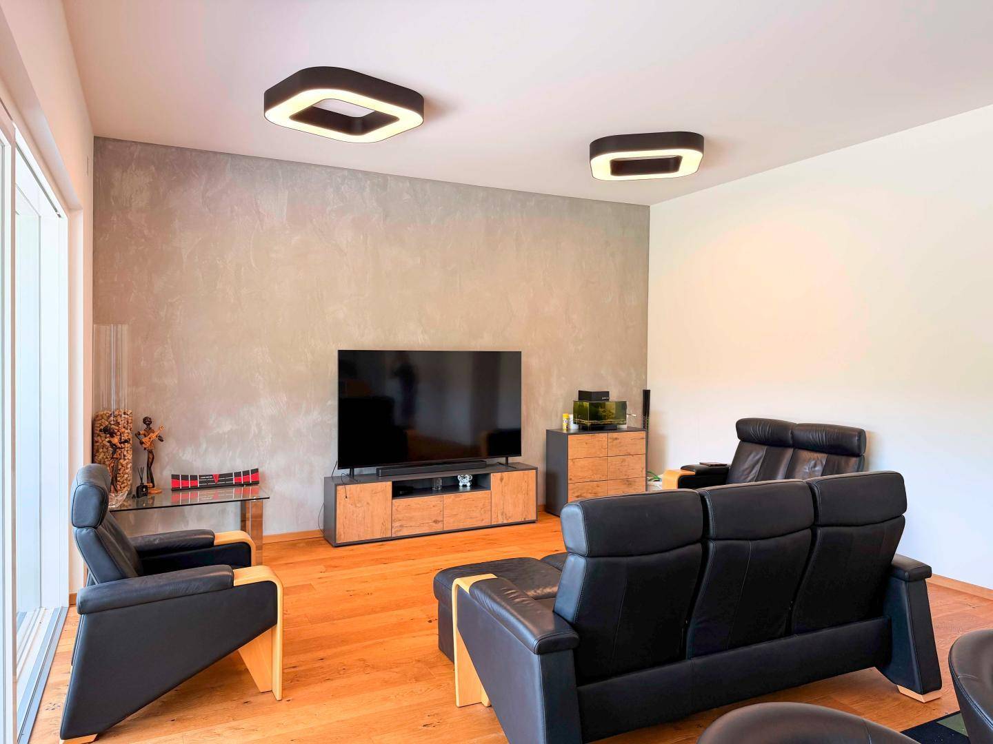 Gemütliches Wohnzimmer mit dunklen Ledersofas, Holzboden und einer strukturierten Akzentwand.