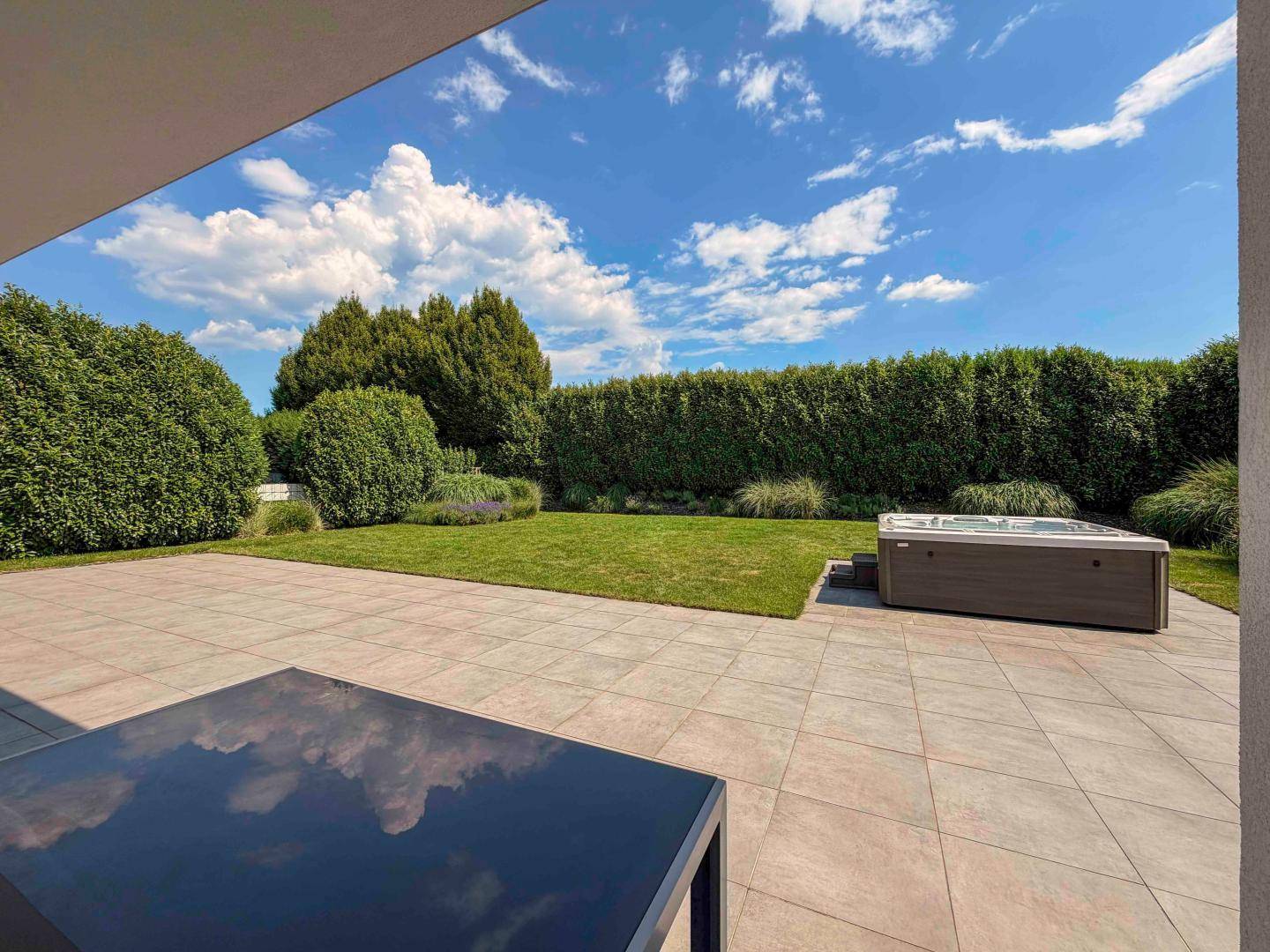 Weitläufige Terrasse mit Whirlpool und umzäuntem Garten, ideal für Entspannung im Freien.