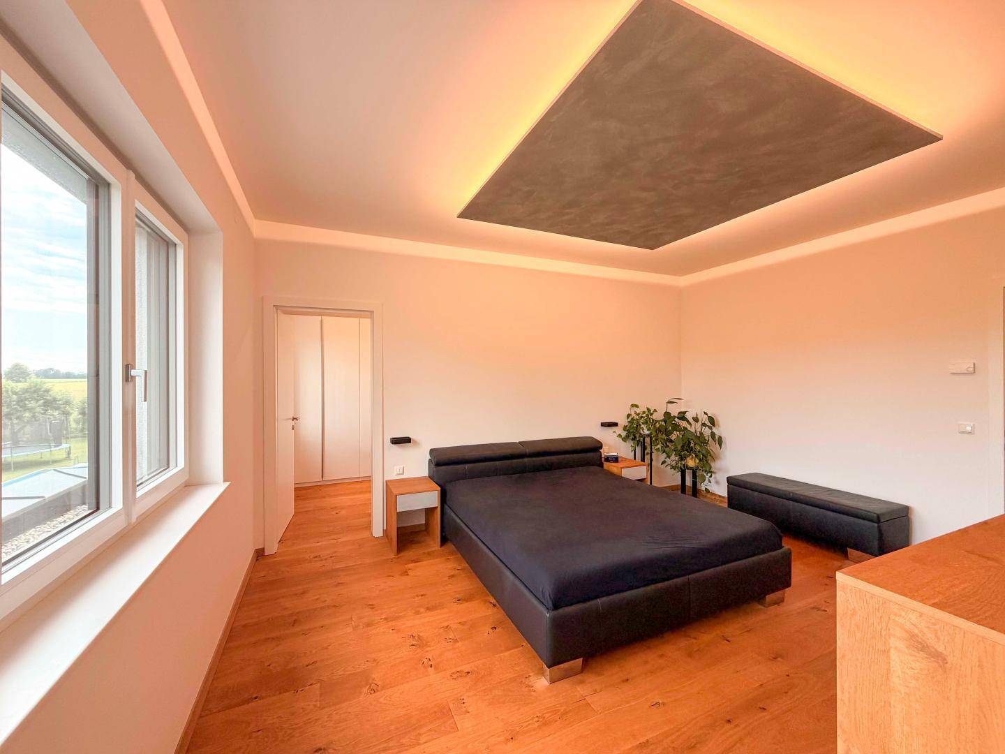 Geräumiges Schlafzimmer mit Holzboden, großen Fenstern und indirekter Deckenbeleuchtung.
