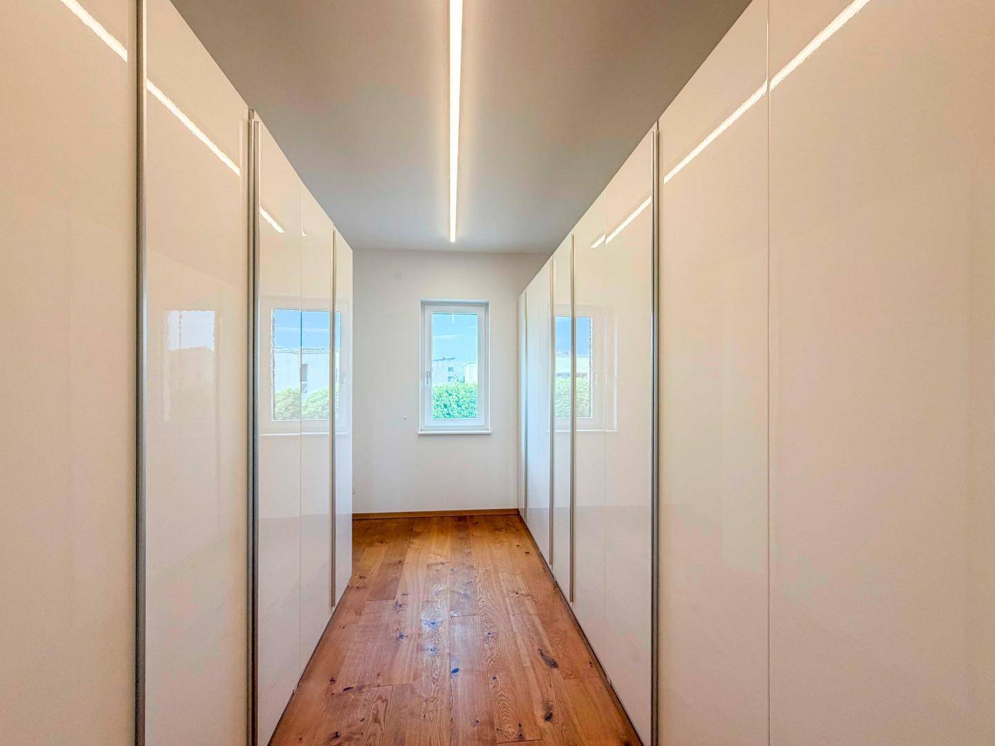Heller Ankleidebereich mit glänzenden Einbauschränken und Fenster für Tageslicht.