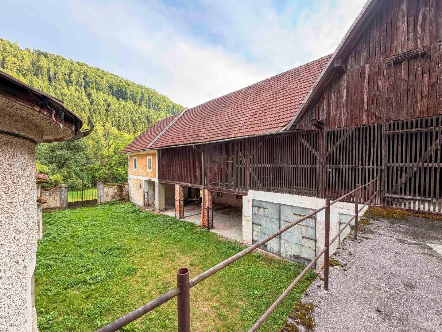 Außenansicht eines Scheunengebäudes mit Holzwänden und rotem Ziegeldach, umgeben von einer Wiese.