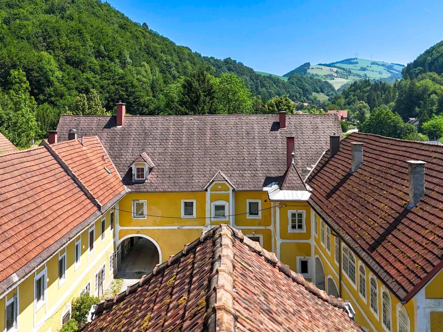 Dachansicht des Anwesens mit roten Ziegeldächern und gelben Fassaden, umgeben von grünen Hügeln.