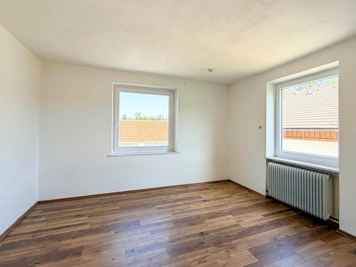 Heller Raum mit Laminatboden und zwei Fenstern, bietet vielseitige Nutzungsmöglichkeiten.