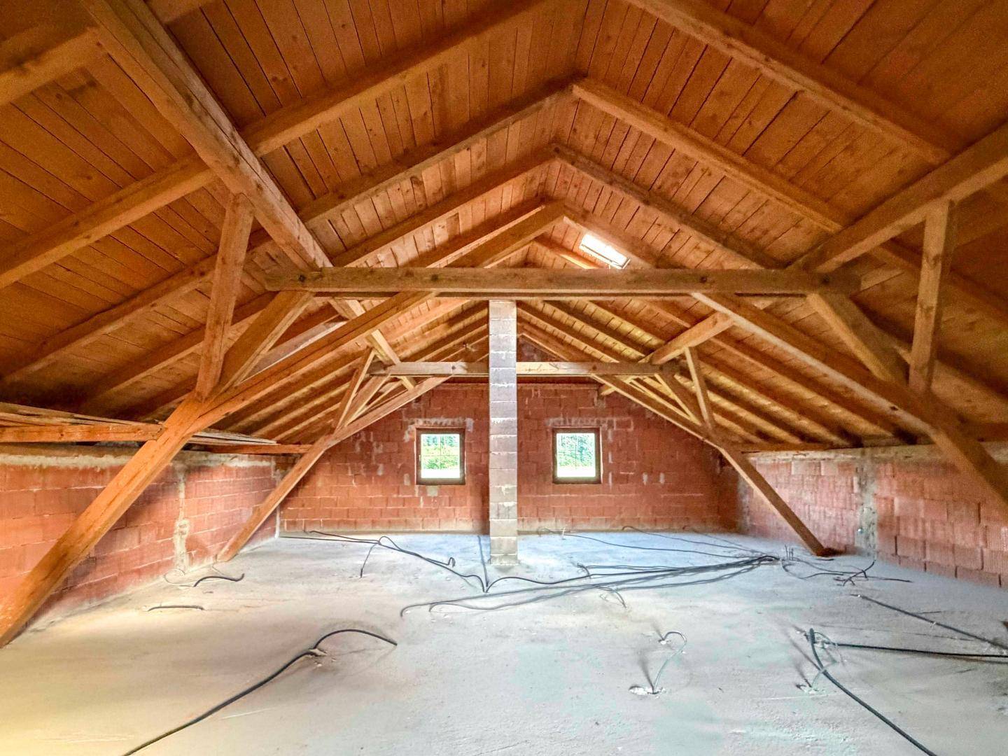 Geräumiger Dachboden mit sichtbaren Holzbalken und Ziegelwänden, bietet Ausbaupotenzial.