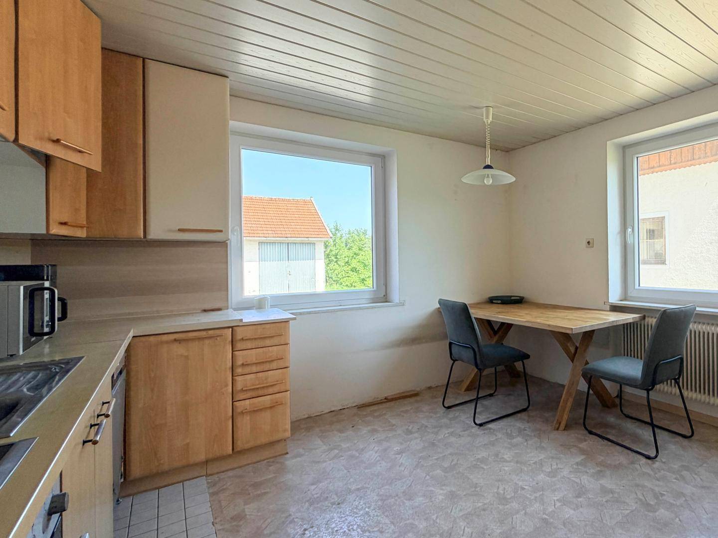 Funktionale Küche mit Holzschränken, Essbereich und Blick ins Grüne durch das Fenster.