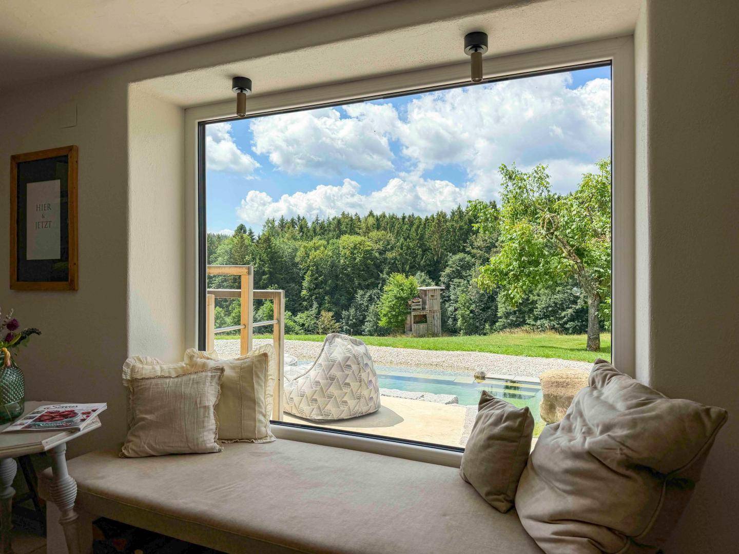 Gemütlicher Fensterplatz mit Kissen und weitem Blick auf den Naturpool und die Landschaft.