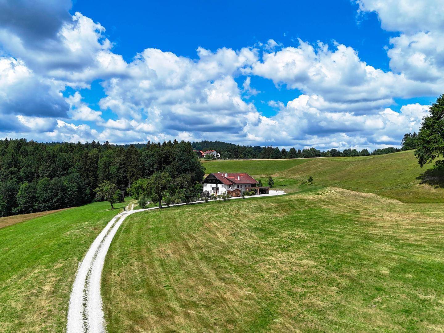 Weitläufige Luftaufnahme eines Landhauses in idyllischer Hügellandschaft mit Feldern und Wald.