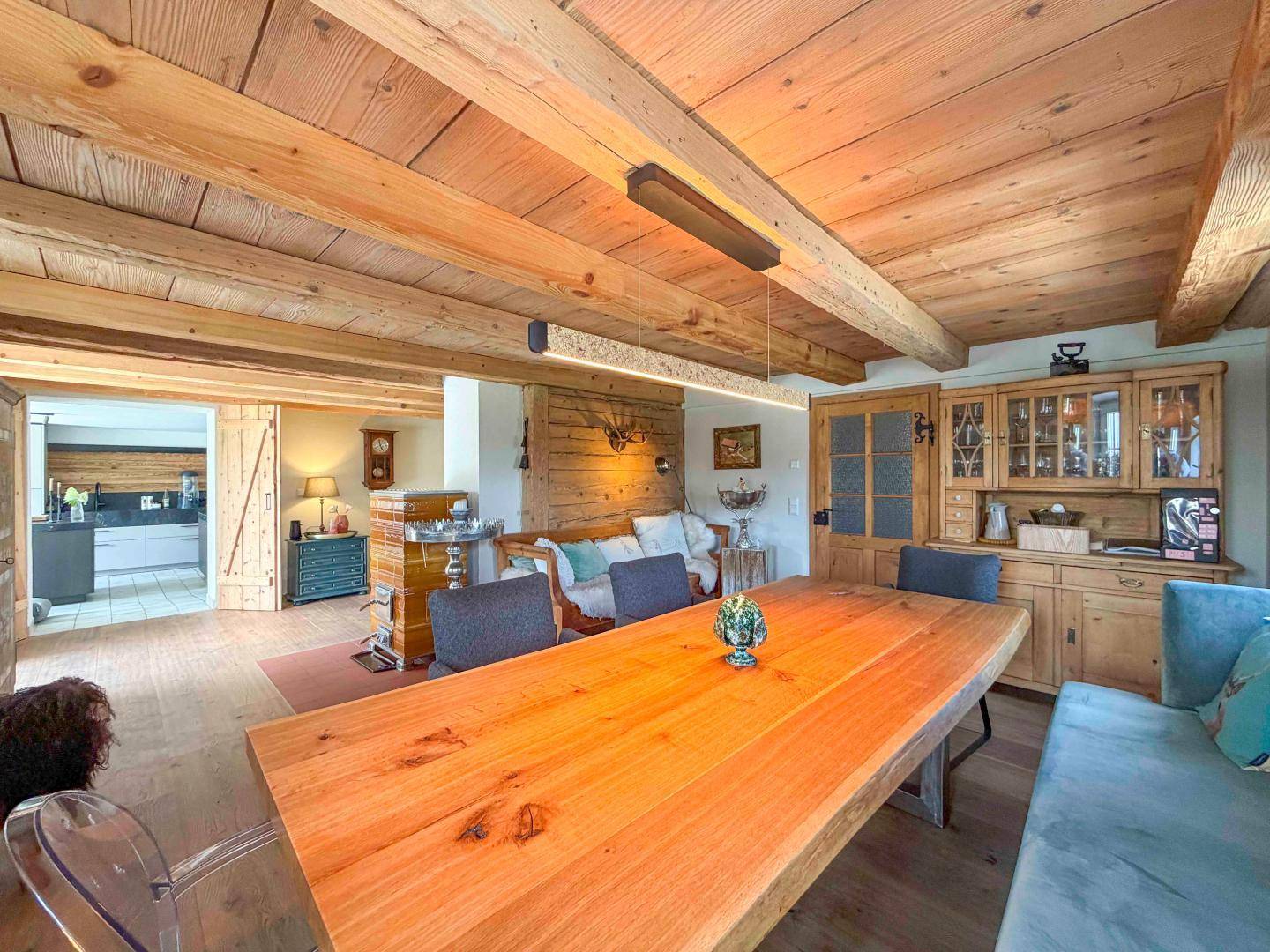 Gemütlicher Essbereich mit großem Holztisch, Holzbalkendecke und offenem Übergang zum Wohnbereich.