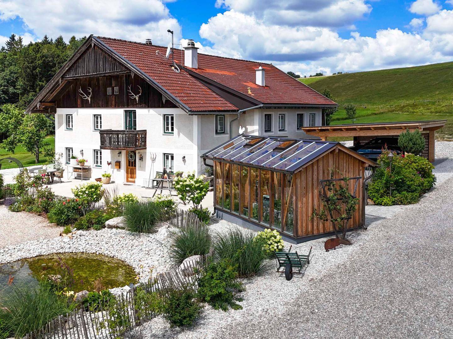 Traditionelles Landhaus mit Gewächshaus, Teich und gepflegtem Vorgartenbereich in ländlicher Umgebung.